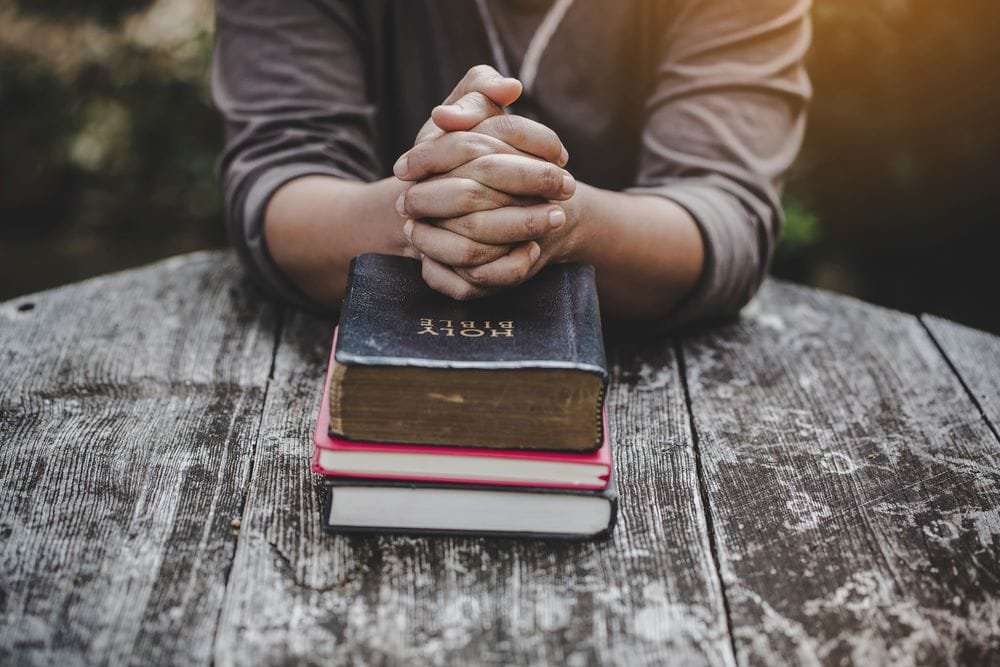 A person with hands folded over their Bible.
