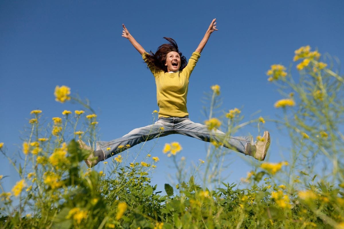 Happy girl rediscovers God's joy as she jumps for joy in a field of flowers.