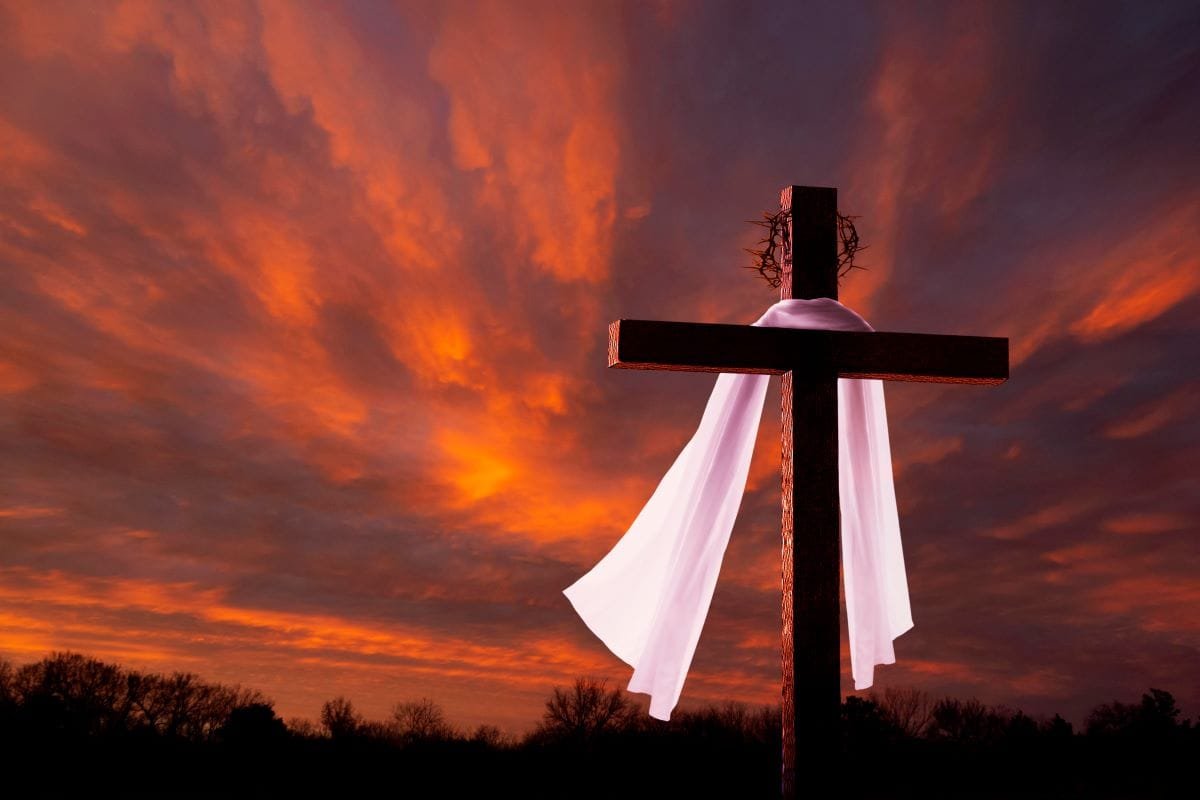 A cross with white linen hanging on it during a beautiful sunset.