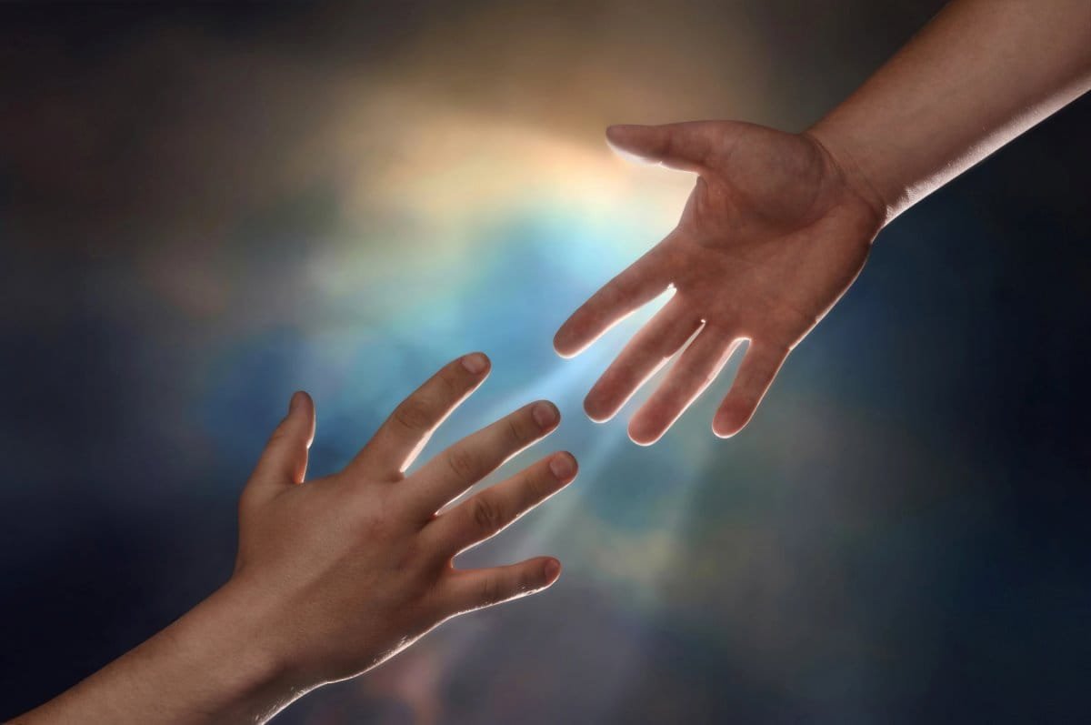 One hand reaches out to another hand to offer help and compassion.