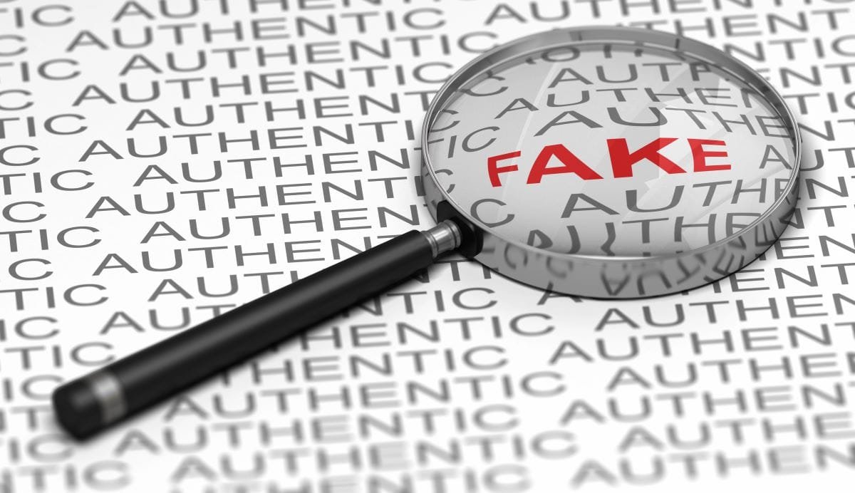 Magnifying lens is over the word Fake in red surrounded by the word authentic.
