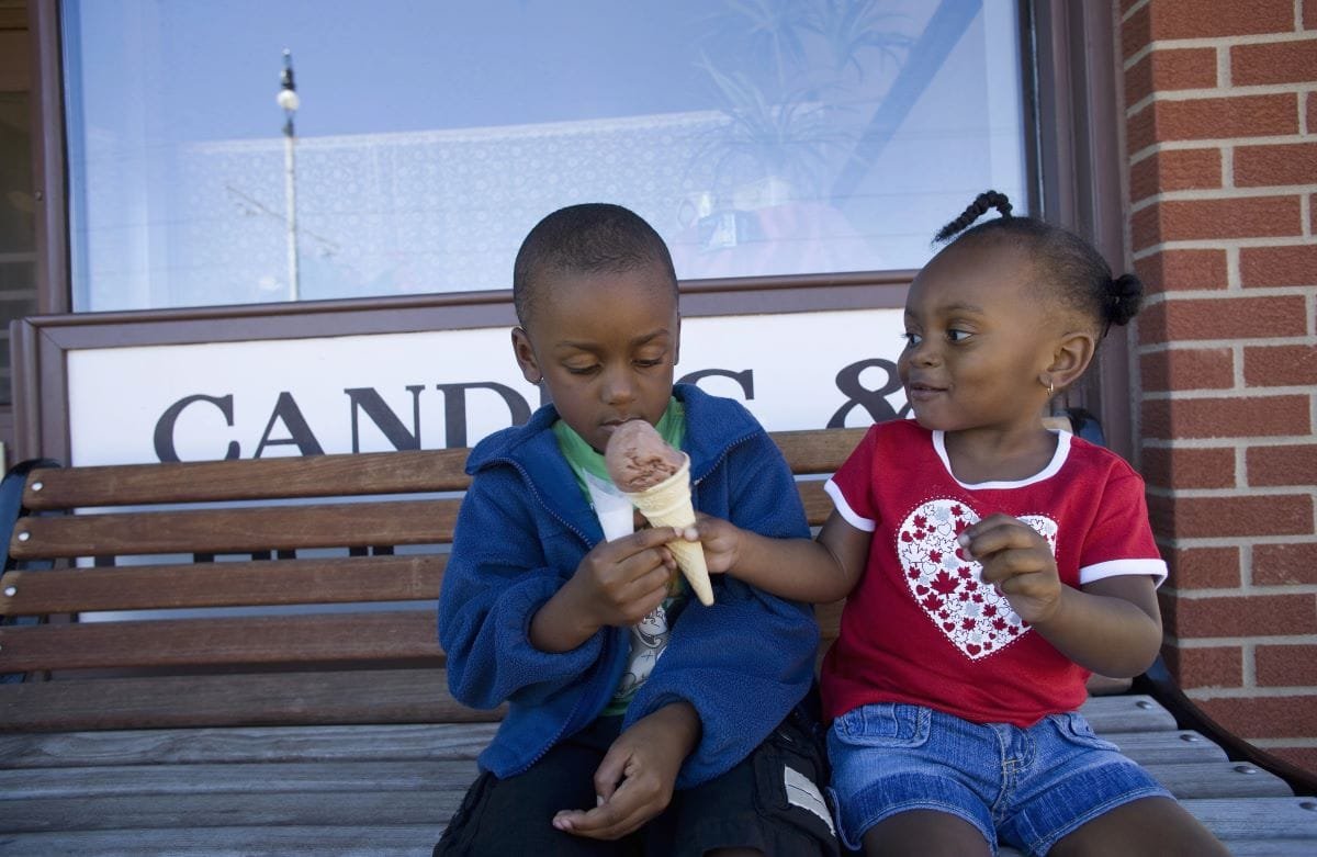 A young child offers an ice cream cone to another.